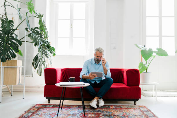 istock Serious senior man using digital tablet, drinking coffee and working at home 2184142362