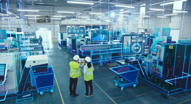 Two Engineers in Safety Gear Use a Tablet to Interact With Holographic Data in a High-tech Factory, Surrounded by Advanced Machinery and Digital Interfaces, Illustrating a Futuristic Manufacturing