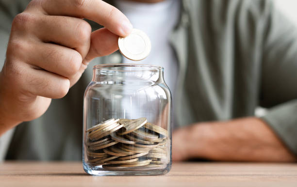 istock Hand Putting Coin in a Jar Full of Coins, Saving Concept 2184146897