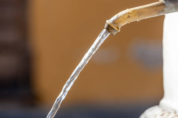 Clear water flows from brass tap, symbolizing purity and hydration in outdoor setting. Captures essence of clean water source, conveying importance in urban areas