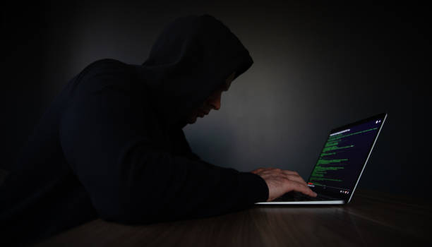 istock A hooded individual is typing on a laptop, with code displayed on the screen, set in a dimly lit room, symbolizing hacking, cybersecurity, or clandestine programming activities. 2184155036