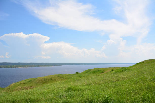 a grassy hill with a lake in the background and blue sky with flying clouds