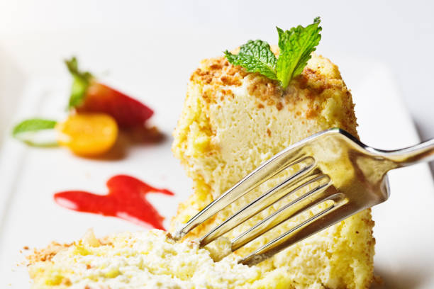 Top-quality cheesecake being sliced by a fork. Served with sweet red sauce and strawberries and kumquats on the side.