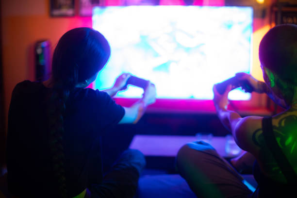 istock Two woman having fun playing video games sitting on the sofa rear view 2184165409