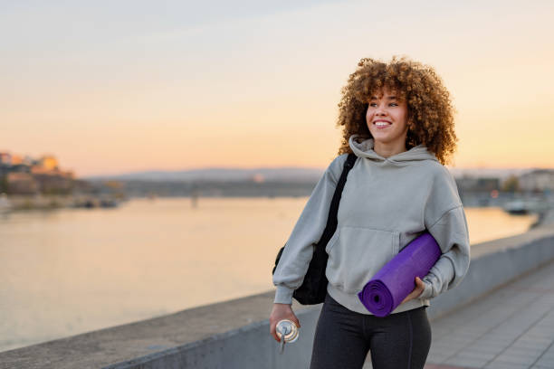 istock Woman holds yoga mat with sunset river background 2184170906