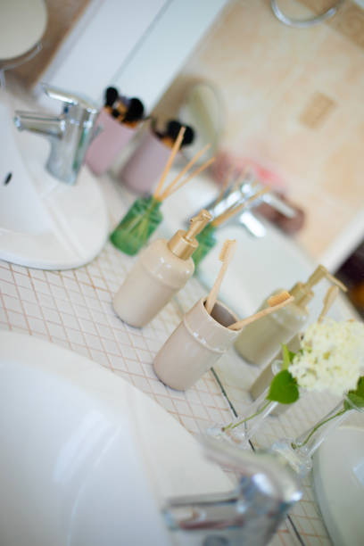 istock Bathroom countertop with arranged toiletries, including bamboo toothbrushes in ceramic holders, soap dispenser, and small vase with flowers, representing cleanliness, eco-friendliness, and minimalism 2184170941