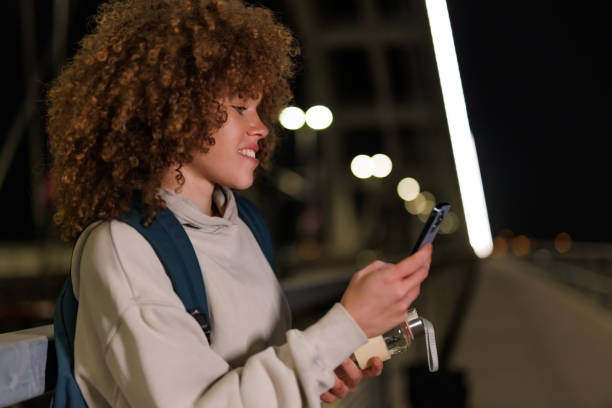 istock Woman with backpack checks phone on illuminated bridge 2184172239