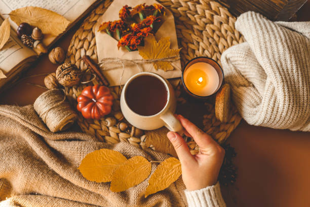 istock Cozy autumn flat lay featuring a warm drink held in hands, surrounded by fall elements such as a candle, pumpkin, twine, dried leaves, and a soft knitted sweater, evoking comfort and seasonal warmth 2184172840