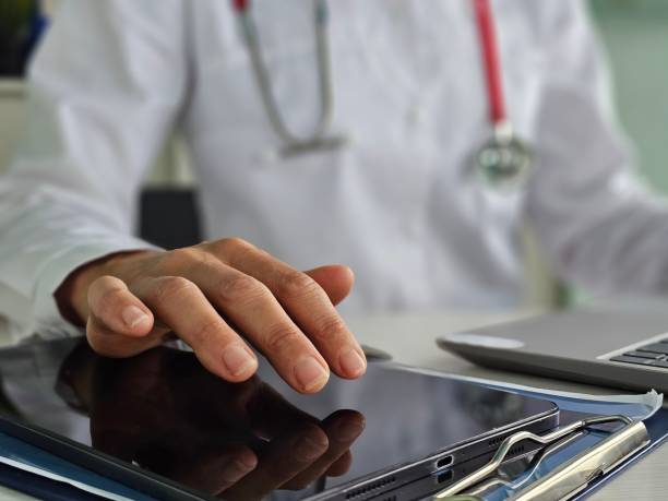 istock Doctor in white coat, hand holding and using modern digital tablet pc, work on laptop computer with stethoscope on the desk at office 2184177809