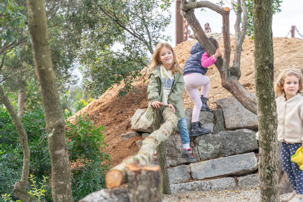 A group of children climbs and explores a nature-filled landscape with trees and rocks. Dressed in casual clothes, they embrace outdoor freedom, curiosity, joy as they engage with their surroundings.