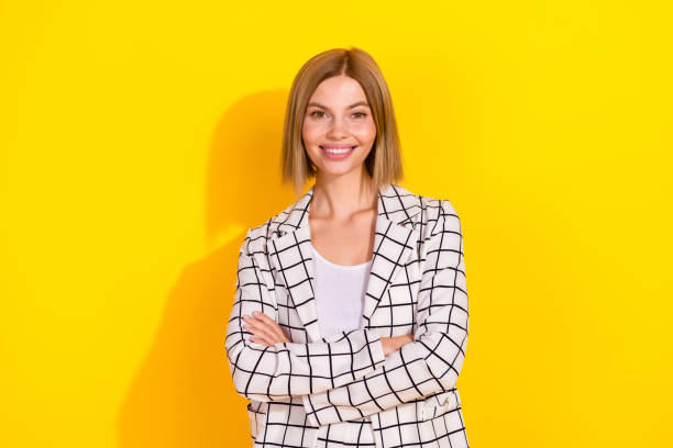 istock Confident woman with a charming smile in a white elegant jacket stands against a bright yellow background expressing success and charm. 2184182531