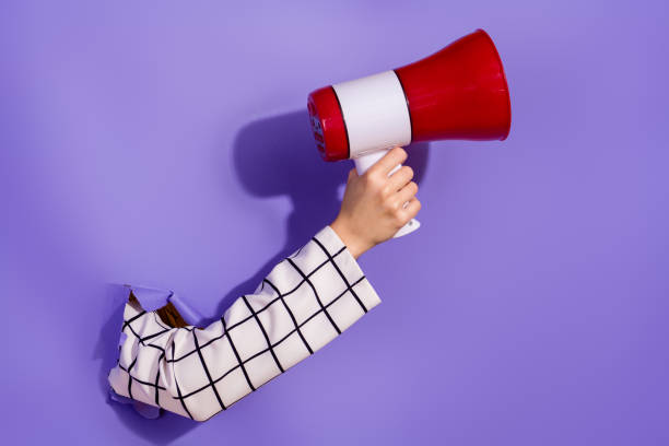 istock Arm holding a megaphone through torn paper on a purple backdrop conveying bold announcement concept 2184182843