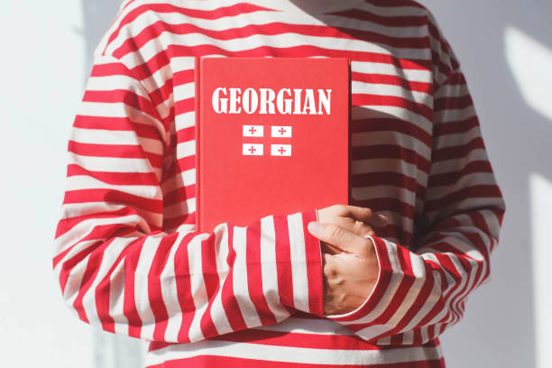 istock One girl, whose face is not visible in a striped red long sleeve, holds a red Georgian language textbook with Georgian flag and Georgian inscription, foreign language learning concept 2184185424