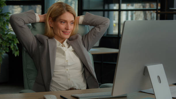 istock Smiling 40s business woman finished computer work stretching sitting at desk in modern office. Happy relaxed middle-aged businesswoman feeling satisfied after online job putting hands behind head 2184189094