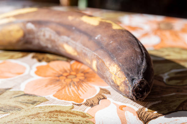 A banana is sitting on a table with a floral pattern. The banana is brown and has a small hole in it