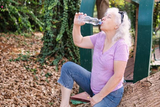 istock Gray-haired elderly lady drinks water from a bottle in the park. 2184197869