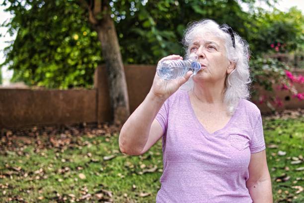 istock Gray-haired elderly lady drinks water from a bottle in the park. 2184197874