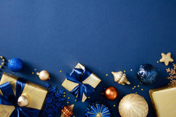 istock Elegant Christmas flat lay composition with luxury gold gift boxes with blue ribbon bows, chic ornaments, baubles, confetti on dark blue background. Flat lay, top view, copy space 2184198283