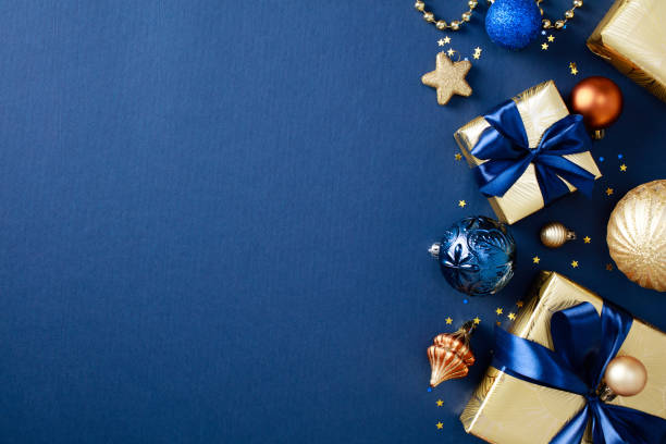 istock Christmas greeting card design. Flat lay golden gift boxes with blue ribbons, assorted Christmas ornaments, and a stars on a deep blue background. Flat lay, top view, copy space 2184198447