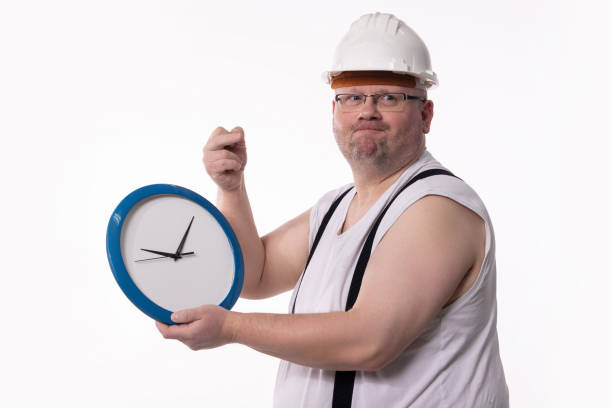 istock A Worker Holding a Clock While Dressed in Construction Gear and Safety Equipment 2184198580
