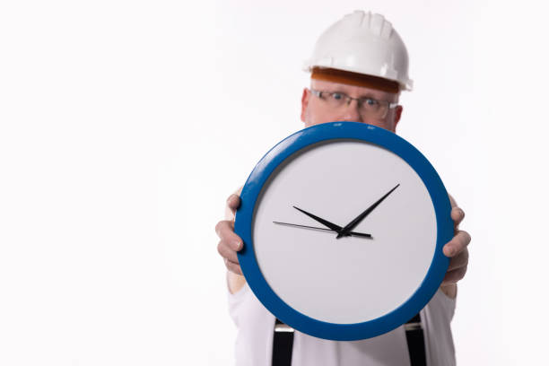 A construction worker in a hard hat holds a clock, symbolizing the importance of time management on site