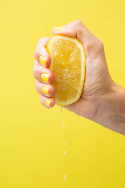 istock A woman's hand with yellow fingernails squeezing half a lemon. 2184209858