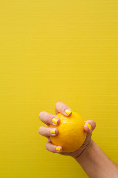 istock A woman's hand with yellow fingernails holding a whole lemon. 2184209890