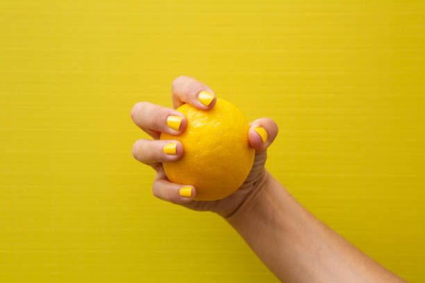 istock A woman's hand with yellow fingernails holding a whole lemon. 2184209894
