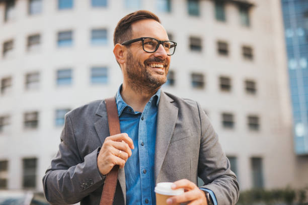 istock Businessman with a takeaway coffee smiling outside on office building 2184210934