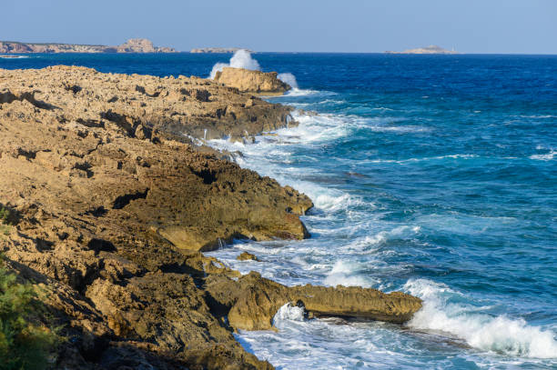Turquoise waves envelop rocky shores, highlighting the beauty of nature on a serene sunny day by the sea.