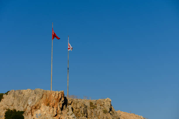 istock Two flags flutter on a rocky outcrop against a clear blue sky under bright sunlight. 2184213346