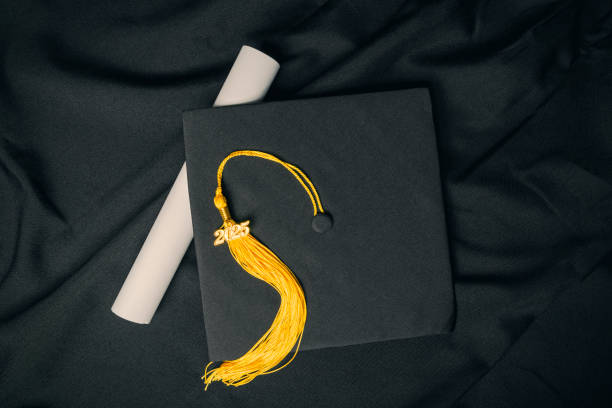 A overhead view of a graduation cap and diploma with a 2025 charm on a yellow tassel.