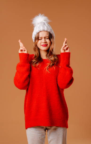 istock Young girl in red sweater and warm hat poses in studio on beige background 2184223621