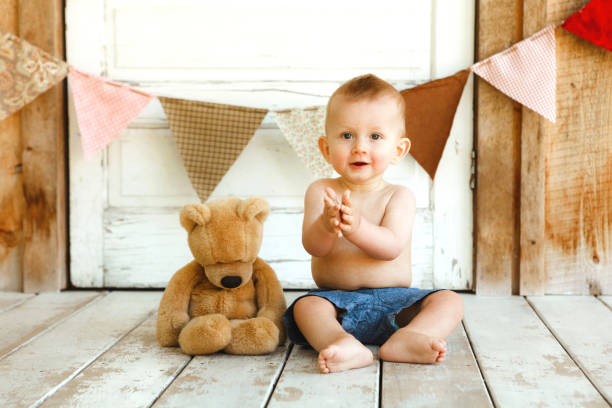A cute baby boy, nine months old, sitting on a porch with a teddy bear.