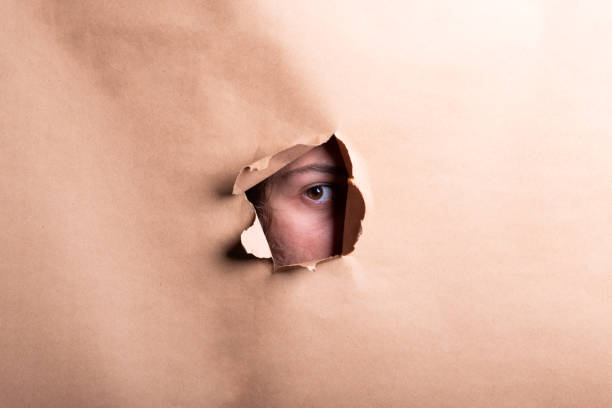 istock Man eye looking through a hole in a sheet of paper. 2184227380