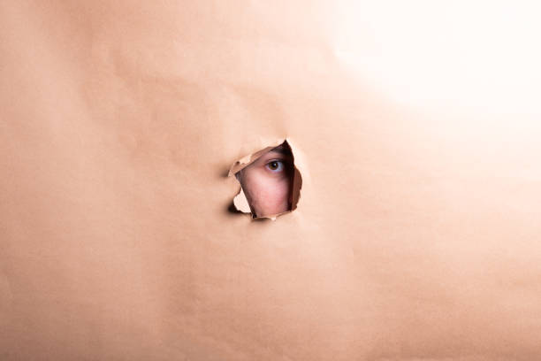 istock Man eye looking through a hole in a sheet of paper. 2184227381