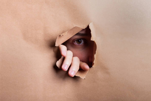 istock Man eye looking through a hole in a sheet of paper. 2184227385