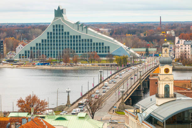 Aerial view of Riga, Latvia, featuring the National Library, a bridge over the Daugava River, visible traffic, and a Ferris wheel in the background.
