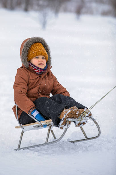 istock Happy boy rides sled on white winter background, snowing 2184234428