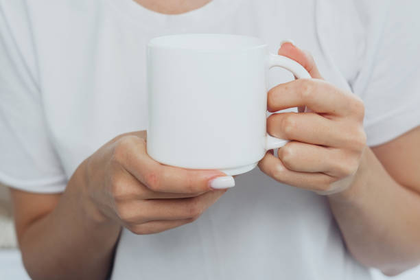 istock A person holding a blank white coffee mug while wearing a simple white shirt indoors 2184238142
