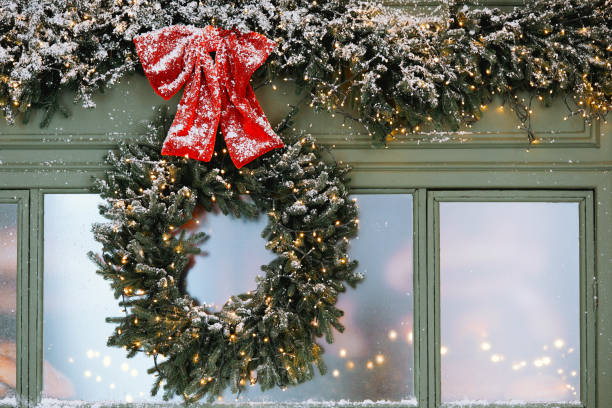 istock Charming winter wreath decorated with red bow and lights on snowy window 2184239822