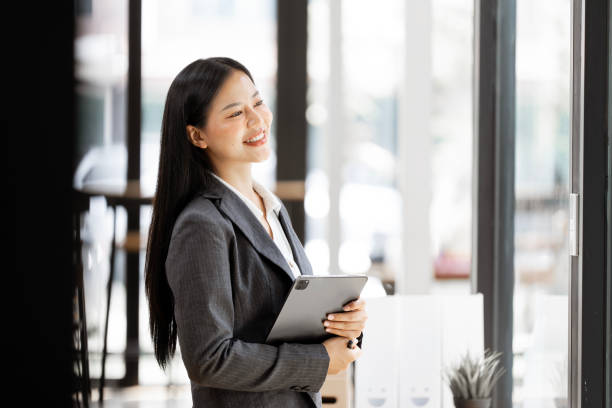 istock Happy female entrepreneur holding tablet while standing in the office and looking up. Copy space. 2184241492