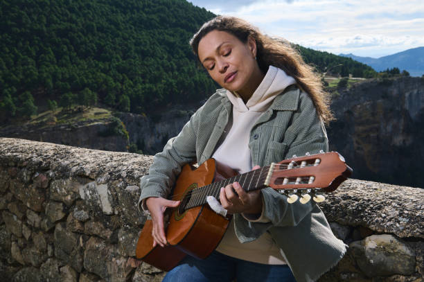Young woman playing guitar by a scenic mountain landscape