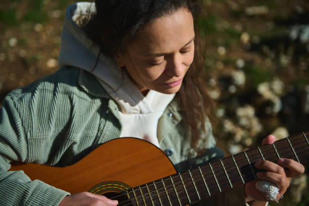 istock Young woman playing acoustic guitar outdoors in serene natural setting 2184252187