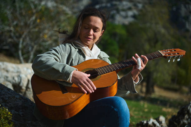 istock Young woman playing acoustic guitar outdoors in a park 2184252200