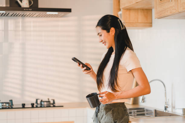 istock woman smiles while checking her phone in modern kitchen, holding coffee cup. warm light creates cozy atmosphere, enhancing her joyful expression. 2184253999