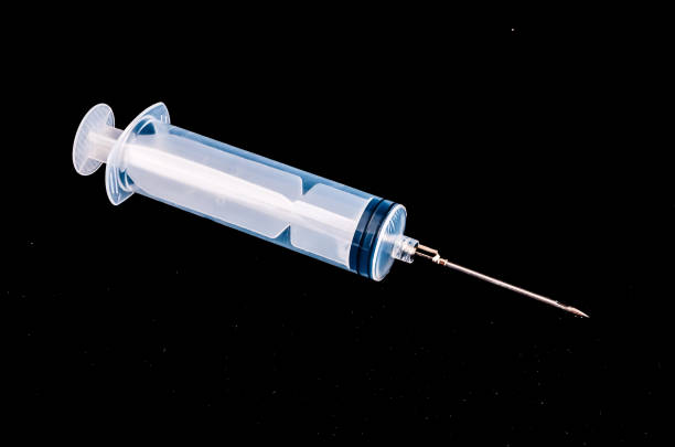 A syringe is shown on a black background. The syringe is clear and has a black rubber stopper