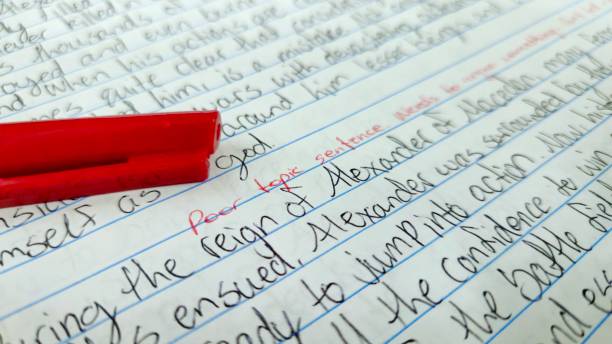 Handwritten essay on lined paper with a red pen placed on top. A marker comment in red ink states, \