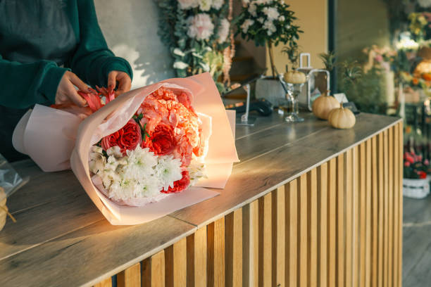 istock Close-up of a luxurious bouquet featuring vibrant red roses, delicate hydrangeas, and white alstroemerias, elegantly arranged and wrapped in soft pastel paper on a wooden counter 2184263362