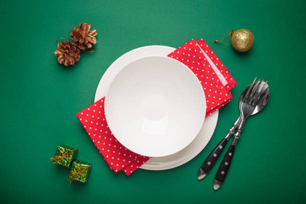 istock Christmas table setting with empty plate, golden pine cones, and red napkin on green background 2184264189